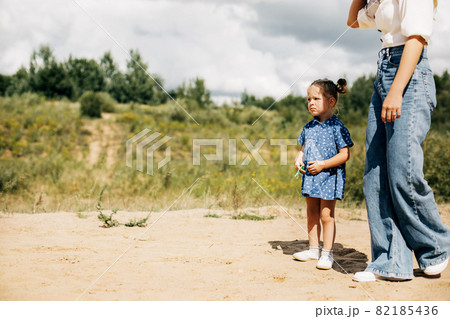 A little girl is standing with her mother on a dirt road 82185436