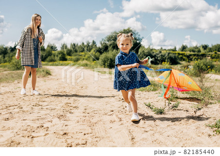 A little girl flies a kite with her older sister and runs away from her 82185440
