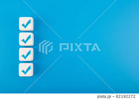 Four blue checkmarks on white cubes in a row against blue background with copy space 82192272