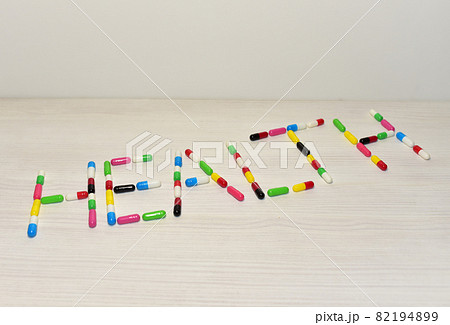 Pills in capsules in the form of the text Health on a table. 82194899