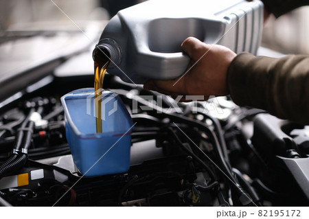 Master repairman pouring motor oil into car engine closeup 82195172