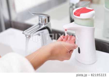 Woman picking up liquid soap from hand dispenser in bathroom closeup 82195223
