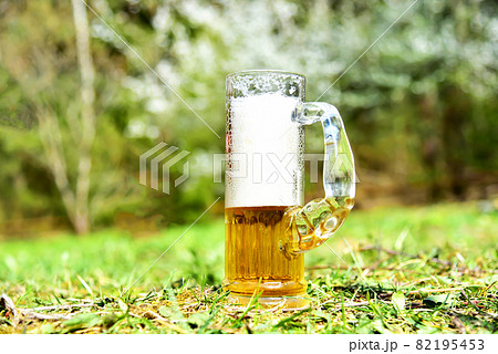 Beer with foam in a large glass glass on the grass in the park against the background of nature Beer with foam in a large glass glass on the grass in the park against the background of nature 82195453