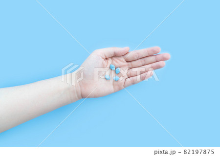 Hands holding sildenafil (Viagra) pills in blister package on blue background. Indication of sildenafil is treatment of erectile dysfunction, pulmonary arterial hypertension. 82197875