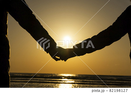 ビーチで夕日を見ながら手をつないでいる親子 82198127