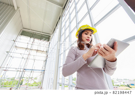 Female engineer in yellow safty helmet is looking to tablet computer 82198447