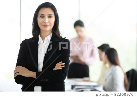 Graceful business woman in black suit standing with dignified manner in office Graceful business woman in black suit standing with dignified manner in office 82200976
