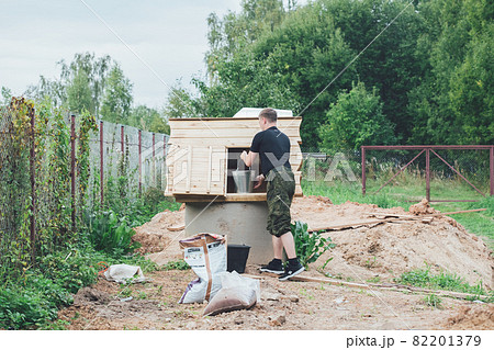 A man collects water into a bucket from a well in a garden plot 82201379