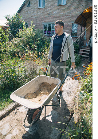 A man carries a garden wheelbarrow for loading sand to fill the paths 82201380