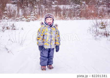 A boy in warm clothes stands in the middle of a winter forest 82201381
