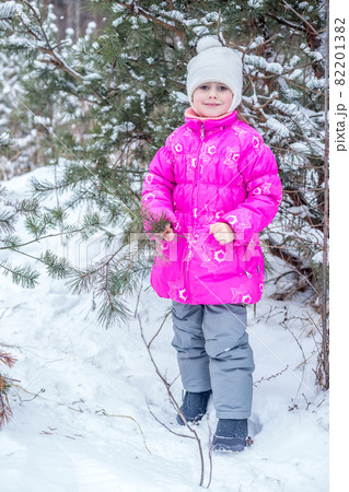 Cute girl in pink warm clothes playing in the winter forest Cute girl in pink warm clothes playing in the winter forest 82201382