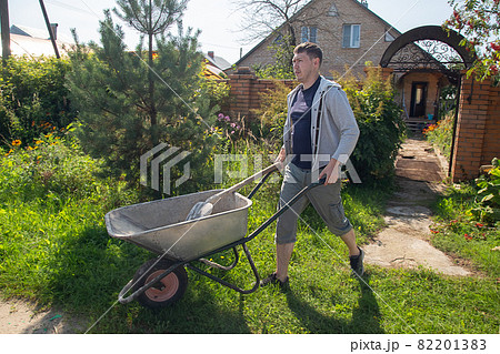 A man carries a garden wheelbarrow for loading sand to fill the paths A man carries a garden wheelbarrow for loading sand to fill the paths 82201383