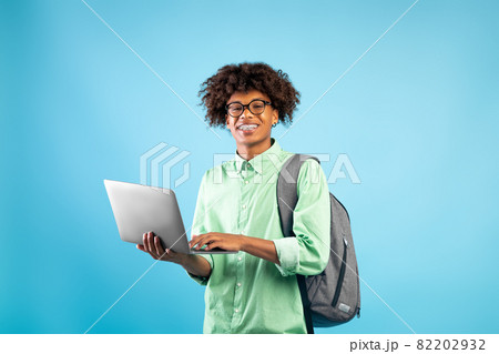 Online education concept. Happy black student guy with backpack and laptop computer, standing over blue background 82202932