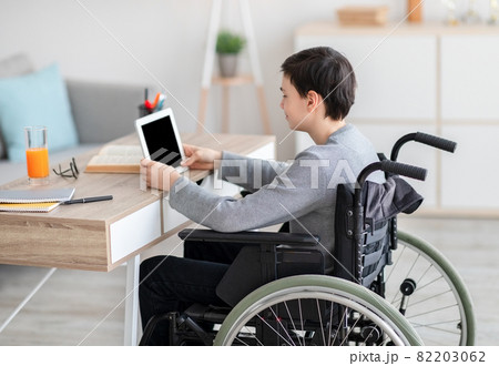 Handicapped teen boy in wheelchair using tablet computer for online education or communication at home Handicapped teen boy in wheelchair using tablet computer for online education or communication at home 82203062