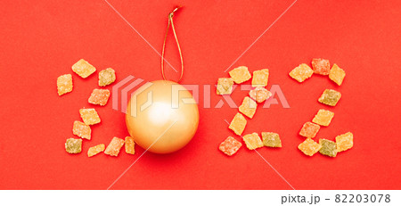 Numeral 2022 from multicolored sweets and golden christmas ball on red background 82203078