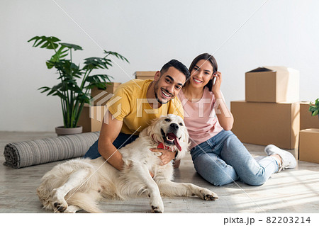 Full length portrait of happy young diverse couple with their dog posing on floor of new home on moving day 82203214