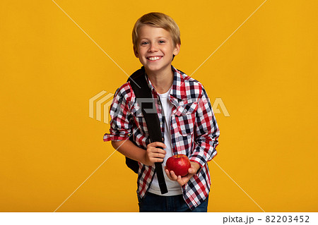 Positive european teenager boy pupil with backpack holding red apple, sharing and look at camera 82203452