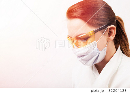 Close up profile Portrait of female doctor wearing a medical mask and yellow protective glasses. Concept of Covid-19 coronavirus quarantine with empty space for text. Close up profile Portrait of female doctor wearing a medical mask and yellow protective glasses. Concept of Covid-19 coronavirus quarantine with empty space for text. 82204123