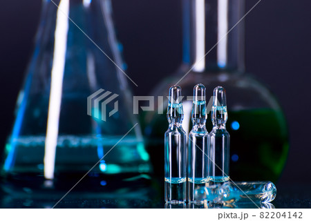 Glass ampoules with liquid for injection against laboratory flasks on dark background. Glass ampoules with liquid for injection against laboratory flasks on dark background. 82204142