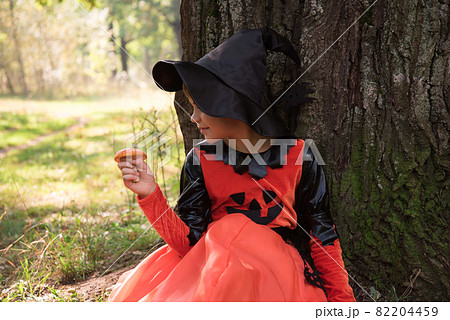 Portrait of a witch. A girl dressed as a witch holds an amanita in her hand. A mushroom for a witch's potion. Beautiful stylish picture in the forest Portrait of a witch. A girl dressed as a witch holds an amanita in her hand. A mushroom for a witch's potion. Beautiful stylish picture in the forest 82204459