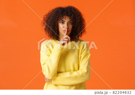Waist-up shot mad and displeased, serious-looking african-american woman telling secret and asking swear not say a word, shushing press index finger to lips and staring angry camera, be quiet 82204632