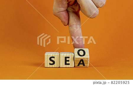 SEO vs SEA. Businessman turns a cube and changs words 'SEA - search engine advertising' to 'SEO - search engine optimization'. Business and SEO or SEA concept. Beautiful orange background, copy space. SEO vs SEA. Businessman turns a cube and changs words 'SEA - search engine advertising' to 'SEO - search engine optimization'. Business and SEO or SEA concept. Beautiful orange background, copy space. 82205925