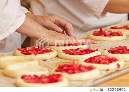 The woman in the picture is making filled fruit pies. Hands filling pie yeast dough with strawberries. Work in the bakery. 82206901