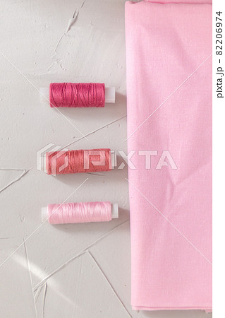 Thread and cotton fabric in pink color against grey background, slow fashion and home sewing concept 82206974