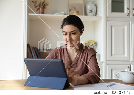 Focused indian female sit at home office use touchpad computer 82207177