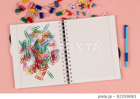 Open school squared notebook and colorful clips on the pink background. Blank white sheet of paper book on the table. Office supplies on the desktop. Back to school. Copy space for text. Top view Open school squared notebook and colorful clips on the pink background. Blank white sheet of paper book on the table. Office supplies on the desktop. Back to school. Copy space for text. Top view 82209063