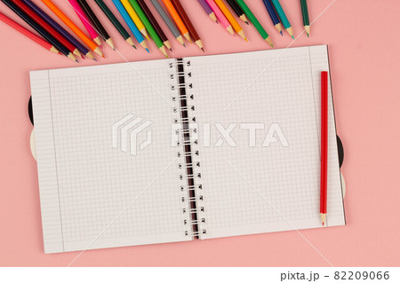 Open school squared notebook and color pencils on the pink background. Blank white sheet of paper book on the table. Office supplies on the desktop. Back to school. Copy space for text. Top view Open school squared notebook and color pencils on the pink background. Blank white sheet of paper book on the table. Office supplies on the desktop. Back to school. Copy space for text. Top view 82209066