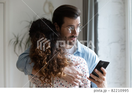 Jealous husband hugging wife and checking her phone 82210995