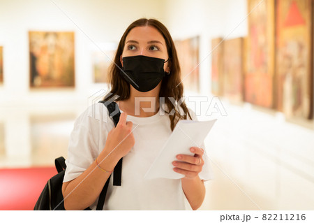 Young girl in a protective mask visits an exhibition of paintings in a museum 82211216