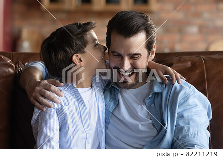Head shot little boy whispering into father ear, having fun Head shot little boy whispering into father ear, having fun 82211219