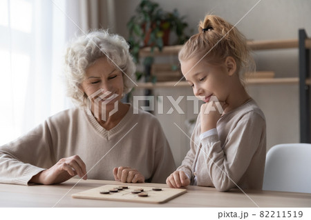 Old grandmother playing draughts with adorable little child girl. Old grandmother playing draughts with adorable little child girl. 82211519