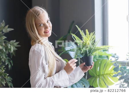 Beautiful woman with blond hair holding plant pot with green leaves in eco office. 82212766