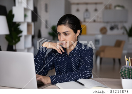 Confident Indian woman working on laptop, looking at screen Confident Indian woman working on laptop, looking at screen 82212873
