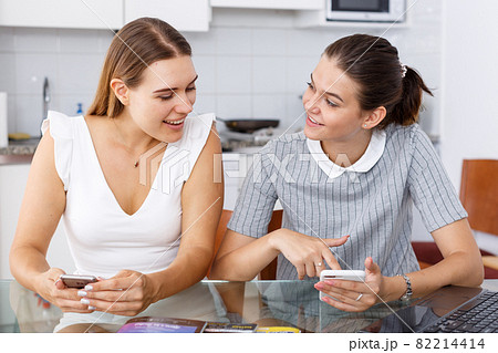 Young smiling girlfriends using phones and chatting table 82214414