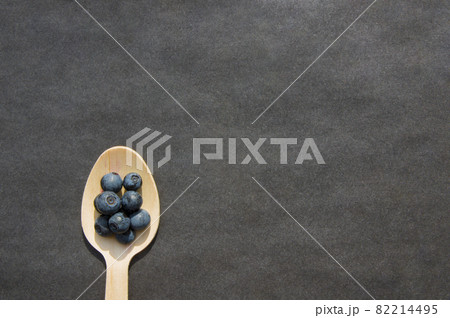 Flat lay of recycled spoon and juicy fresh blueberries on rough table. Space for text. Isolated ripe sweet bilberry fruits in eco spoon on black background. Copyspace. Healthy raw vegetarian food Flat lay of recycled spoon and juicy fresh blueberries on rough table. Space for text. Isolated ripe sweet bilberry fruits in eco spoon on black background. Copyspace. Healthy raw vegetarian food 82214495