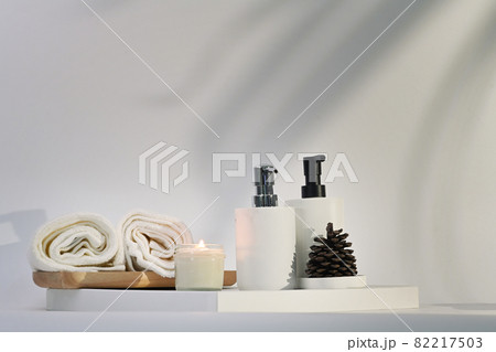 Burning aromatic candle, towels and shampoo bottles on white table. Spa accessories. 82217503
