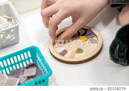 Master class on making mosaic panels. Close-up of the hands of a girl student taking a piece. 82228274