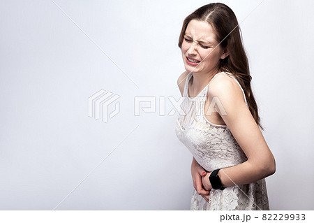 woman with freckles and white dress and smart watch with stomach pain on silver gray background. woman with freckles and white dress and smart watch with stomach pain on silver gray background. 82229933