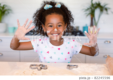 Happy african american girl baking in kitchen, showing hands messy with dough 82245596