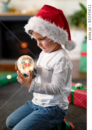 Focused caucasian boy wearing santa hat, looking at snow globe at christmas time 82245611