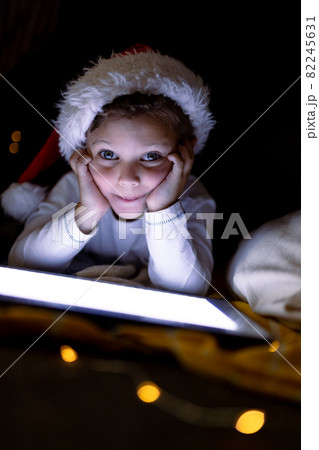 Caucasian boy wearing santa hat, using tablet, looking at camera at christmas time Caucasian boy wearing santa hat, using tablet, looking at camera at christmas time 82245631