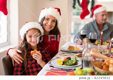 Happy caucasian mother and daughter wearing santa hats looking at camera at christmas time 82245632