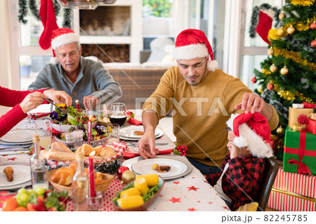 Caucasian multi generation family wearing santa hats having christmas meal Caucasian multi generation family wearing santa hats having christmas meal 82245785