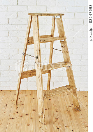 白いレンガの壁の前に置かれたアンティークな木製脚立の写真素材