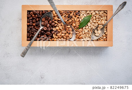 Green and brown decaf unroasted and dark roasted coffee beans in wooden box with scoops setup on white concrete background. with scoons setup on white concrete background. Green and brown decaf unroasted and dark roasted coffee beans in wooden box with scoops setup on white concrete background. with scoons setup on white concrete background. 82249675
