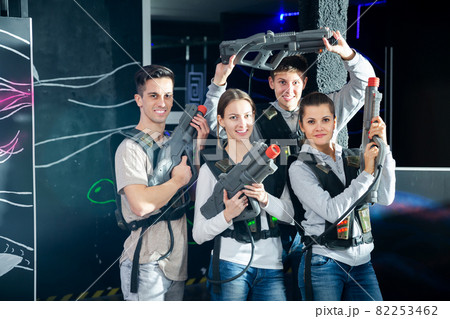 Four happy young men an women posing with laser pistols in their hands in dark laser tag room 82253462